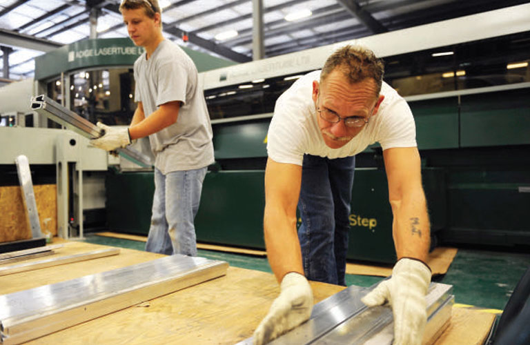 Two SixAxis employees handle cut rectangular tube emerging from one of the company’s two tube lasers.